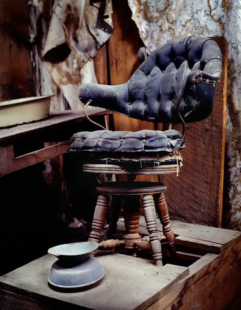 der einsame, historische hydraulische Barbierstuhl von Joe Hahner mit rissigem Bezug im staubigen Innenraum neben der Sam Leon Bar in Bodie