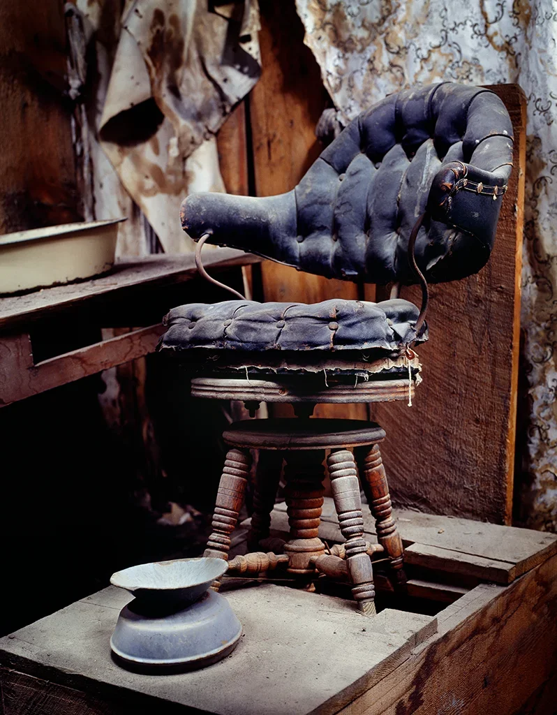 der einsame, historische hydraulische Barbierstuhl von Joe Hahner mit rissigem Bezug im staubigen Innenraum neben der Sam Leon Bar in Bodie