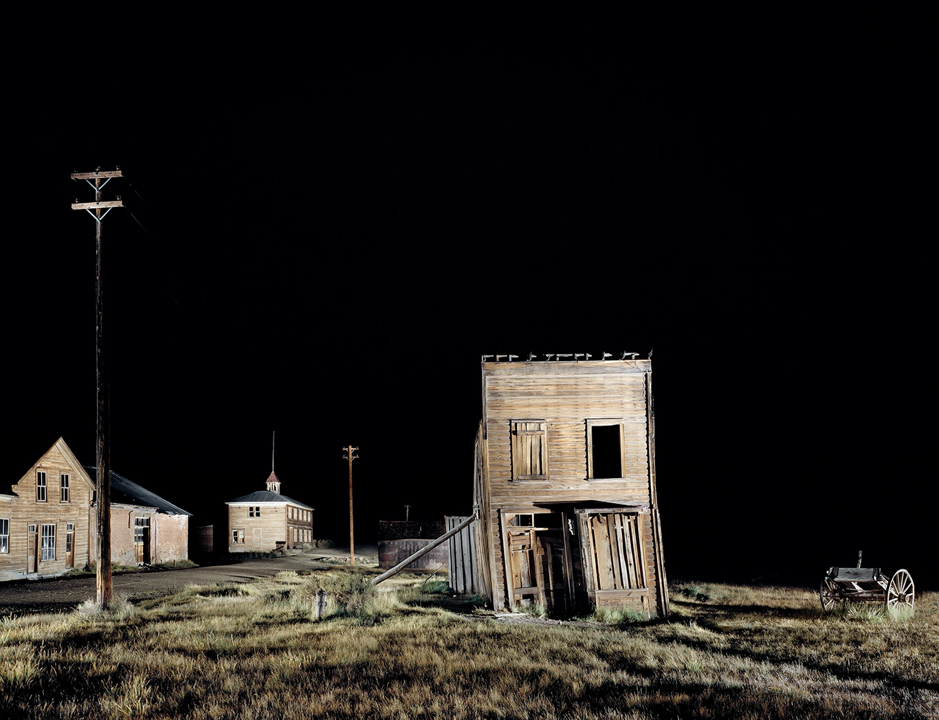 ein in der Nacht beleuchtetes windschiefes Holzhaus in der Ghost Town Bodie