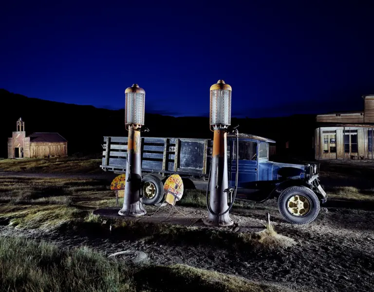 blauer historischer Dodge Graham Truck von 1927 an einer Shell-Tankstelle mit gläserner Zapfsäule vor einem hölzernen Feuerwehrhaus in Bodie