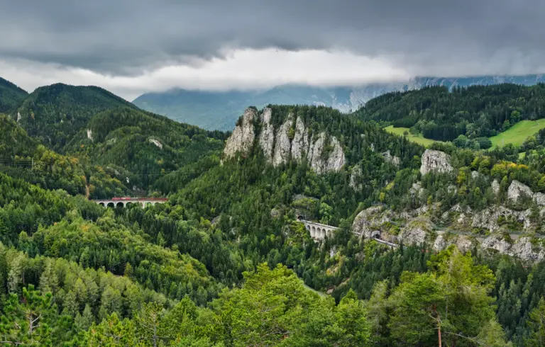 20-Schilling Blick auf das monumentale, zweigeschossige Kalte-Rinne-Viadukt der Semmeringbahn aus Ziegelmauerwerk. Die Brücke schmiegt sich elegant an die bewaldeten Hänge der Polleroswand. Im Hintergrund ragt das wolkenverhangene, raue Raxmassiv in den Himmel
