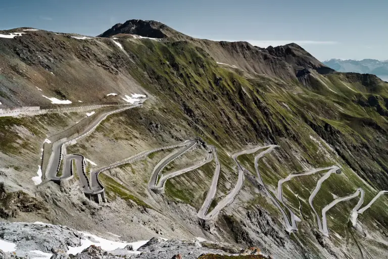 Blick auf die Ostrampe der Stilfser-Joch-Straße mit zahlreichen Serpentinen im Morgenlicht; historische Alpenstraße mit steiler, kurvenreicher Trassenführung.