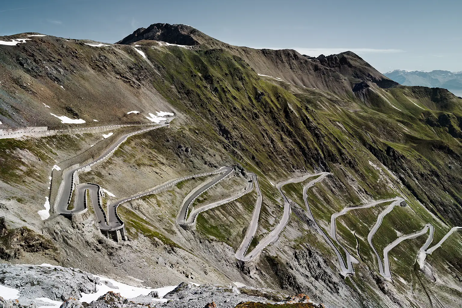 A view of the eastern approach to the Stelvio Pass road, with its numerous hairpin bends in the morning light; a historic Alpine road with a steep, winding route.