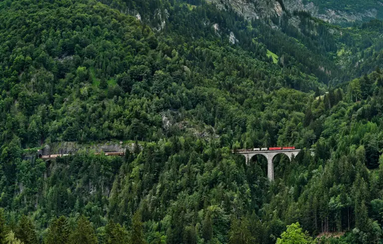Güterzug auf der Schmiedtobelbrücke an der Westrampe der Arlbergbahn inmitten der steilen Wald- und Berglandschaft in Vorarlberg