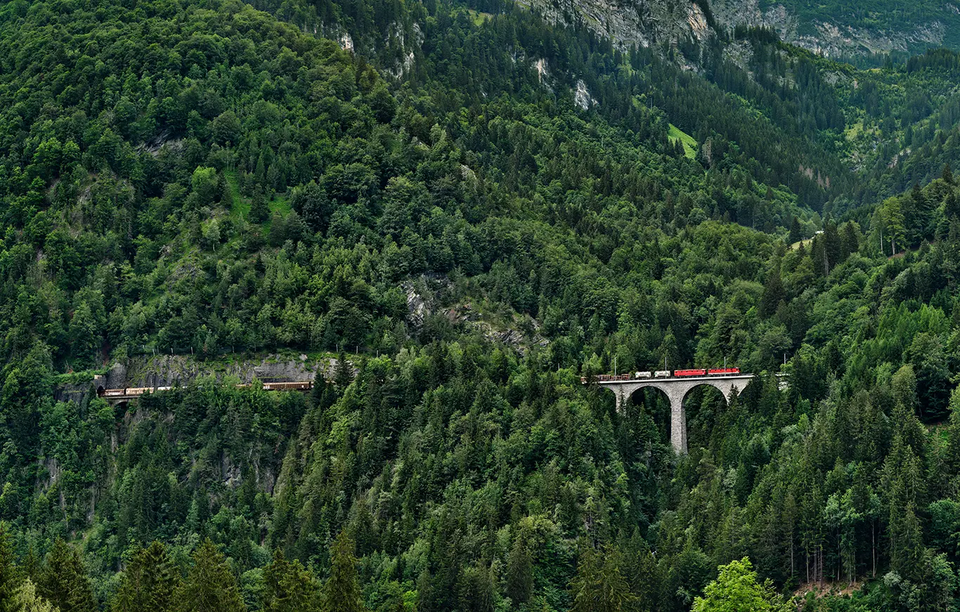 Güterzug auf der Schmiedtobelbrücke an der Westrampe der Arlbergbahn inmitten der steilen Wald- und Berglandschaft in Vorarlberg