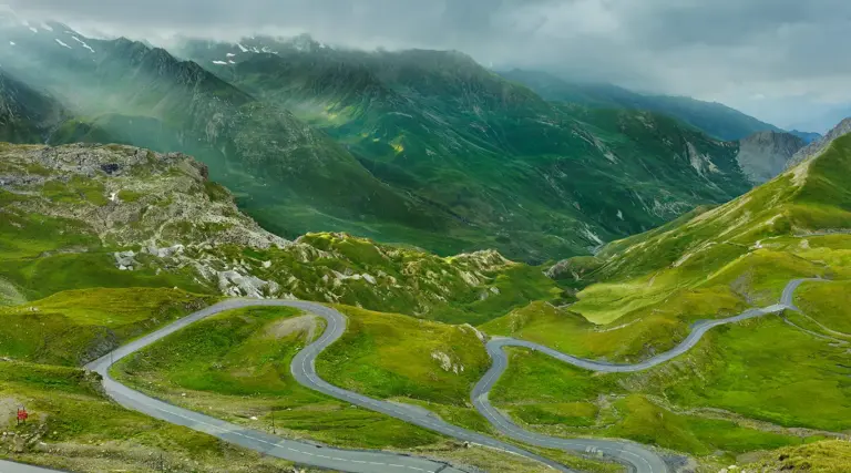 Straße des Col du Galibier zwischen sommergrünem Gras in einer kargen, oft windgepeitschten Passlandschaft