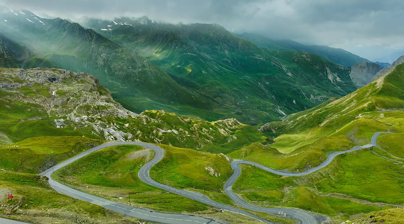 Straße des Col du Galibier zwischen sommergrünem Gras in einer kargen, oft windgepeitschten Passlandschaft