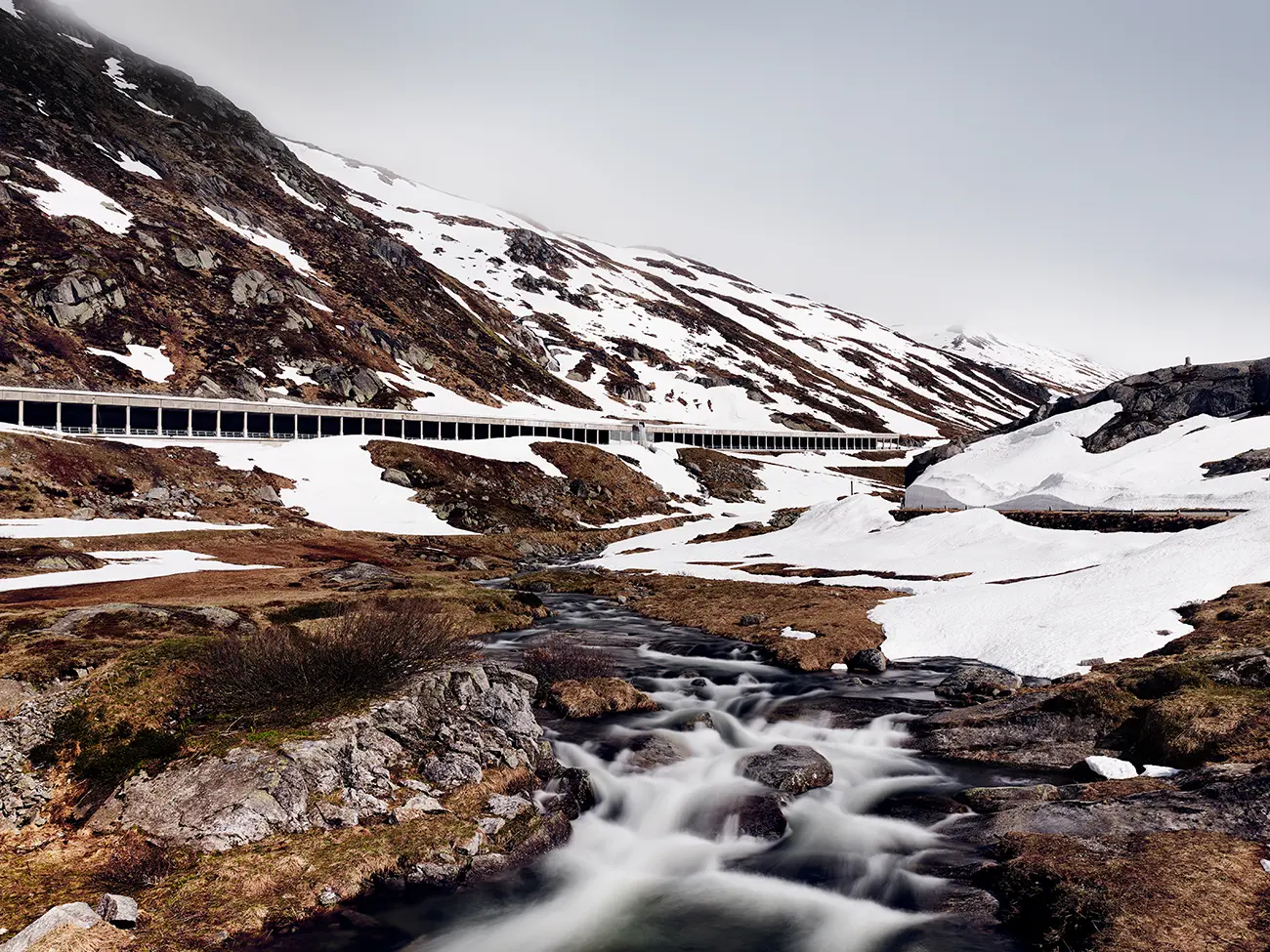 Neue Passstraße durch die Galleria Scaglioni an der Nordrampe des St. Gotthard Pass nach der Wintersperre, Gotthardreuss fließt durch die schmelzenden Schneefelder
