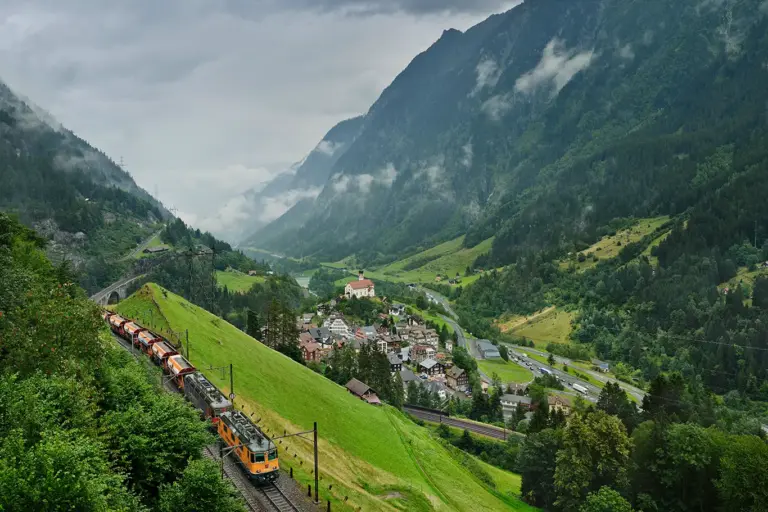 ein Güterzug mit oranger Lok unterwegs auf der obersten der drei Gleisebenen der Gotthardbahn bei Wassen