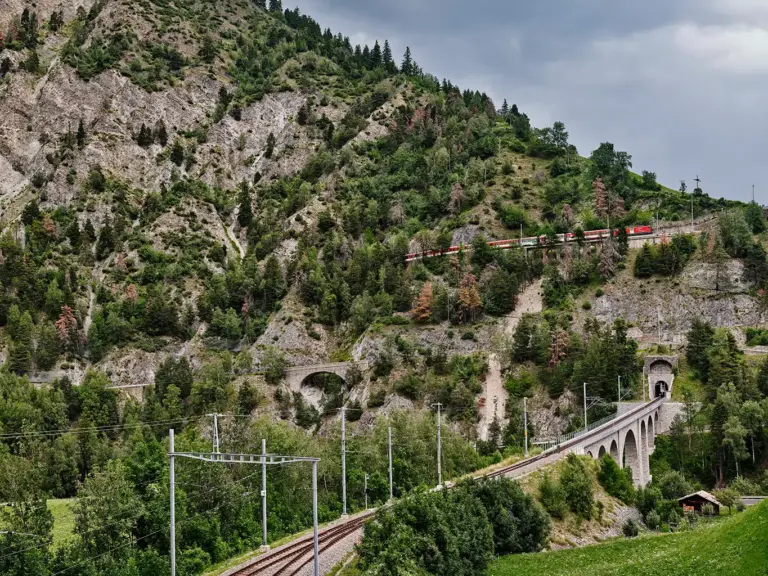 Berglandschaft am Grengiols Kreiskehrtunnel mit Blick auf unteres Tunnelportal, darüber ein Zug der Matterhorn-Gotthard-Bahn