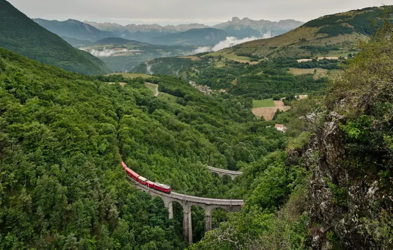 roter Zug der wiederbelebten La Mure Bahn auf dem oberen Loulla Viadukt inmitten von Wäldern und vor der Bergkette des Vercors Massiv