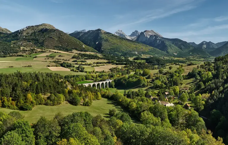idyllische Landschaft an der Bahnstrecke Ligne des Alpes mit Blick zum Viaduc des Fauries, wo gerade ein Zug quert