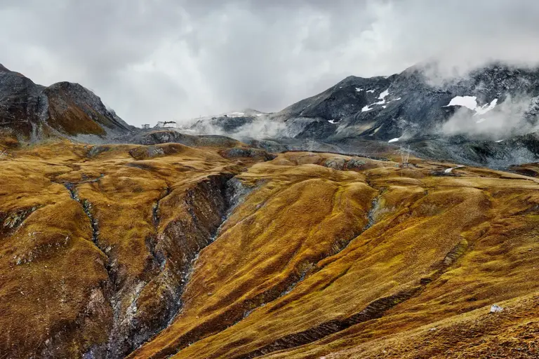 Wolkenverhangen, das rotbraune Herbstgras am Wegrand, der Blick vom Umbrailpass hinauf zur Passhöhe des Stilfser Jochs, 2757 Meter